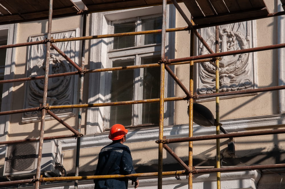 Construction worker in orange safety helmet stands on scaffolding while historic building wall restoration